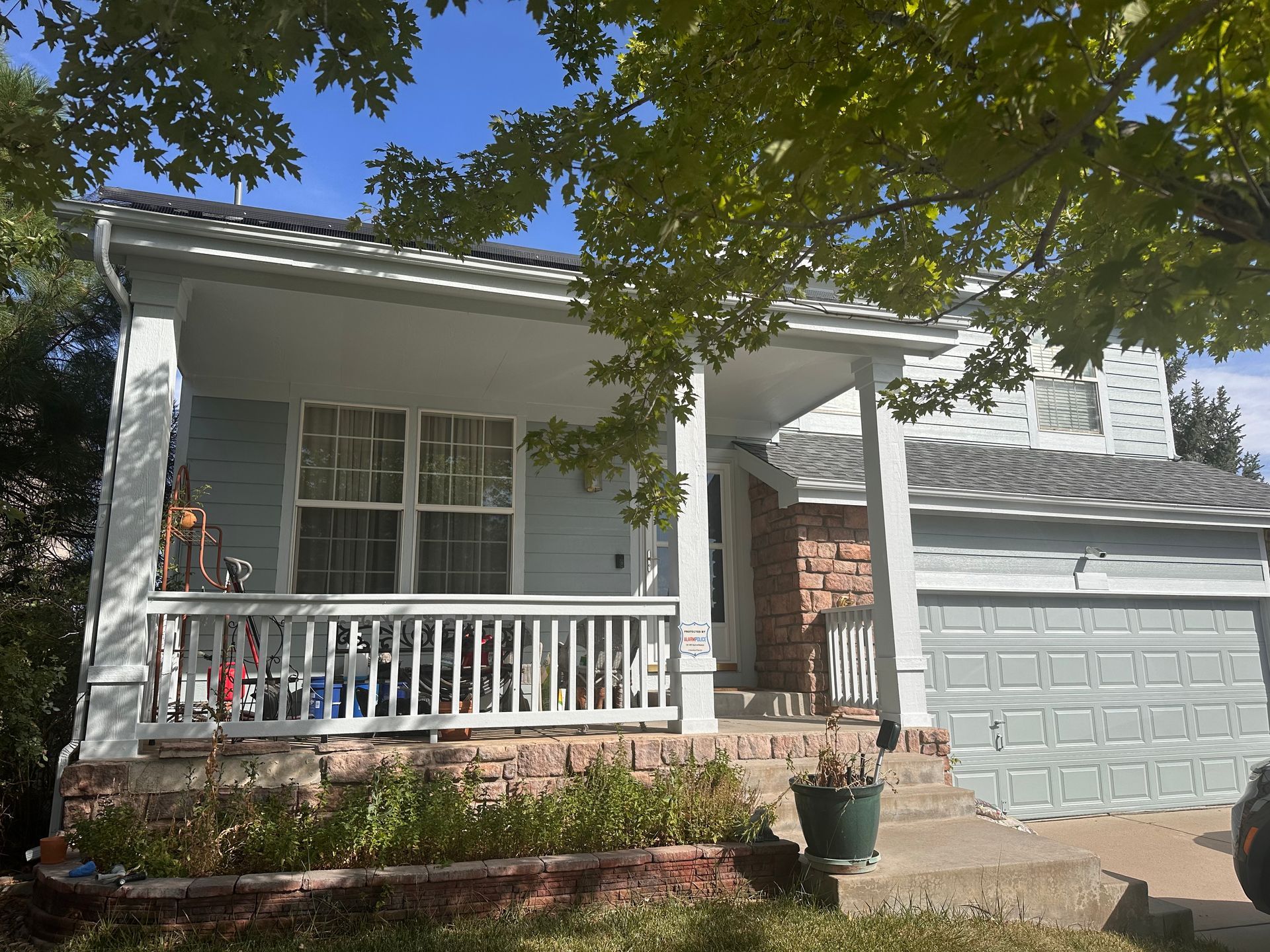 Light blue house with a porch, garage, and a tree. Brick accents, gray roof.