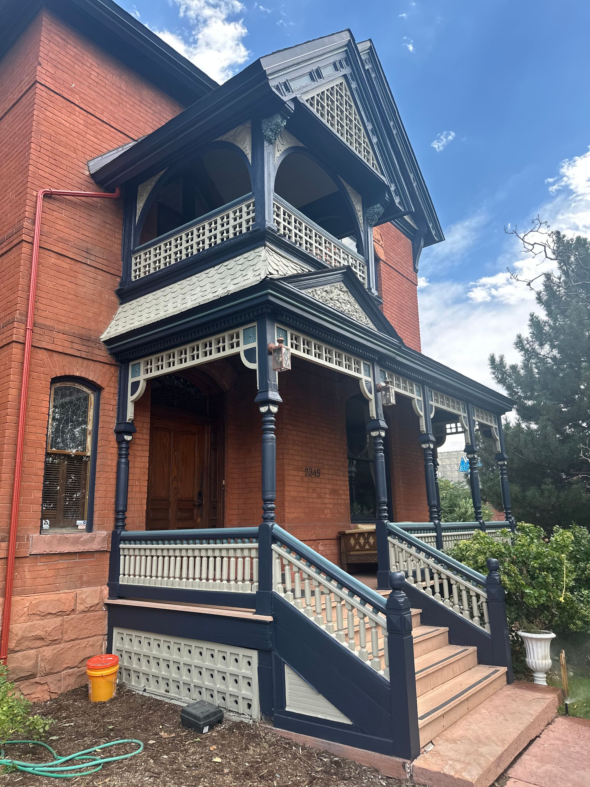 Brick house with dark blue and white ornate porch and balcony.