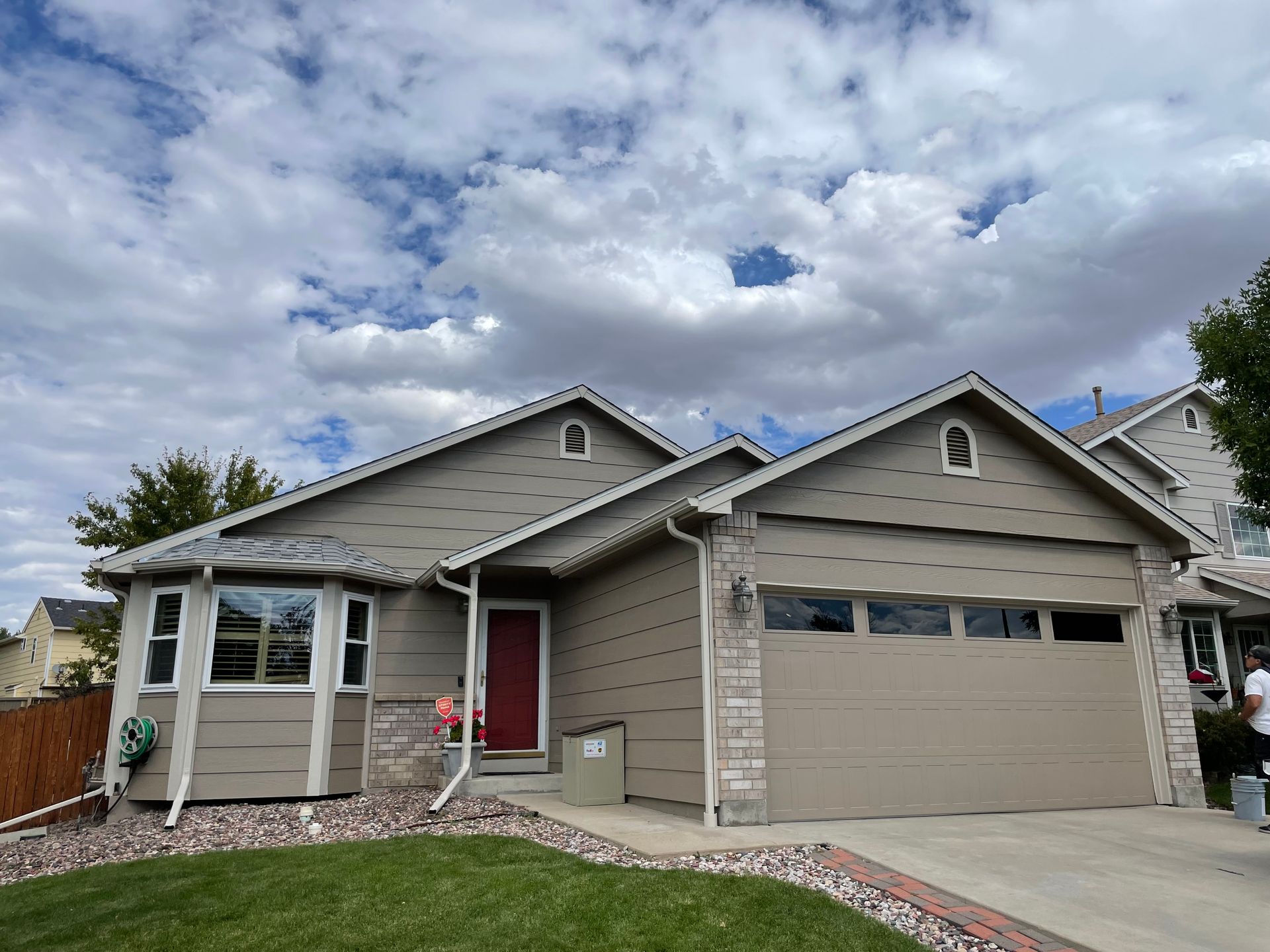 A tan house with a red door, stone accents, and a garage door, set under a cloudy sky.