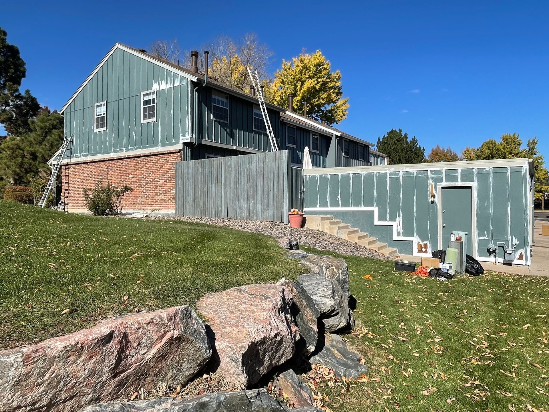 House with peeling blue siding and a red stone foundation; ladder leaning against the roof.