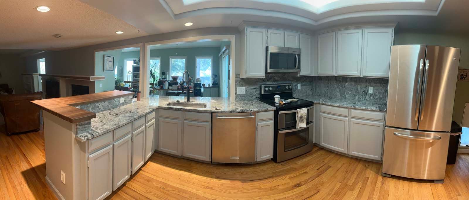 A modern kitchen with a large island, gray cabinets, and stainless steel appliances. Hardwood floors.