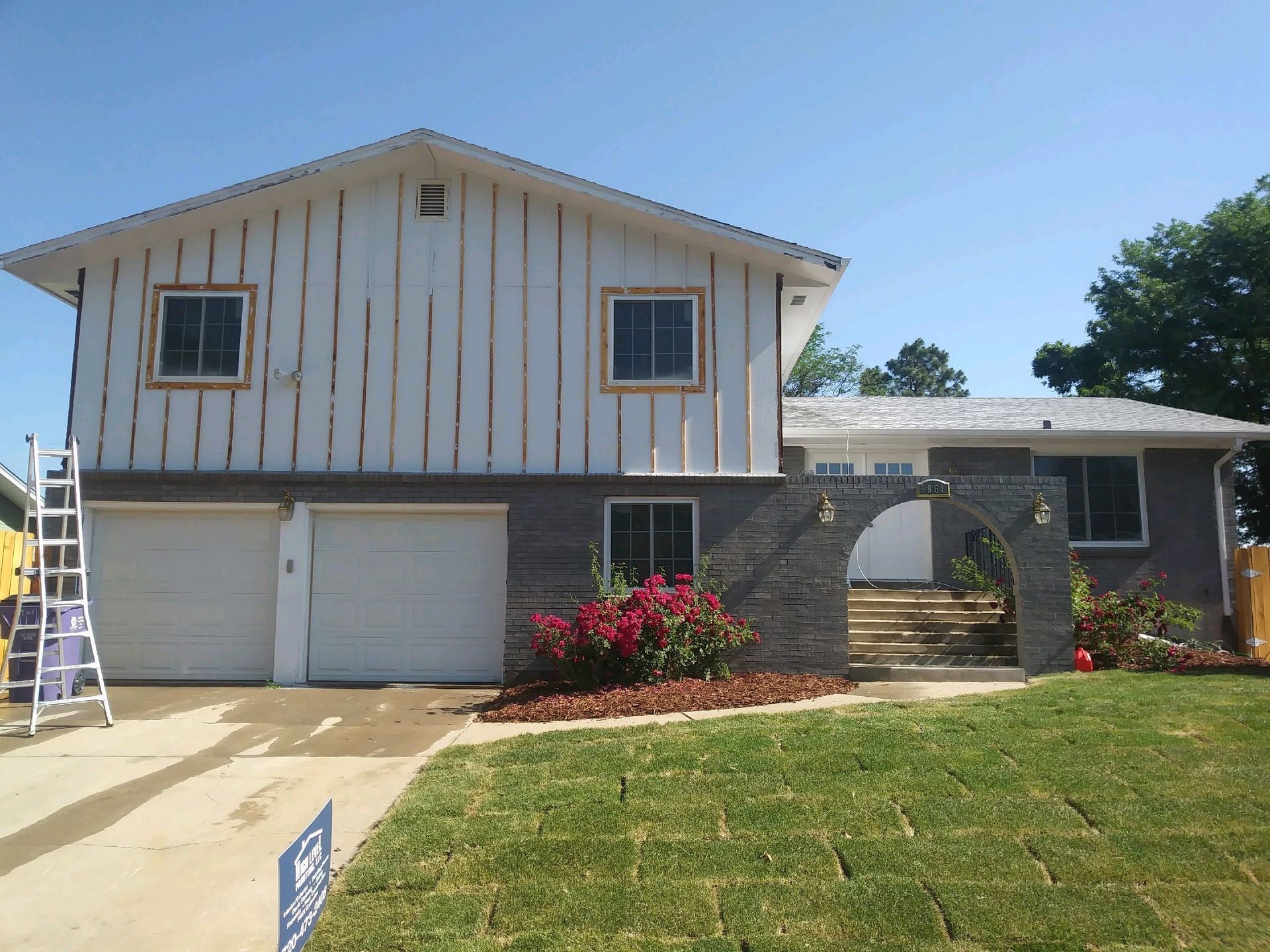 Two-story house with white upper siding, gray brick lower, and an arched entrance.
