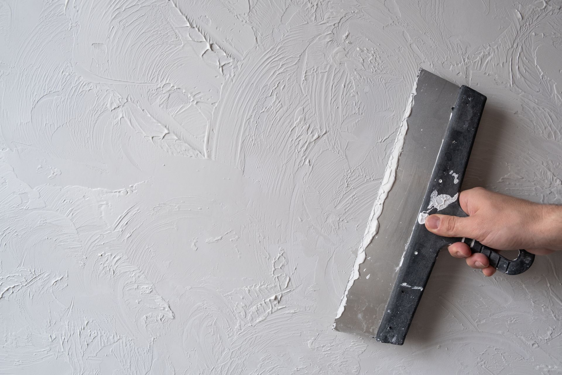 Hand using a trowel to apply plaster on a gray wall.