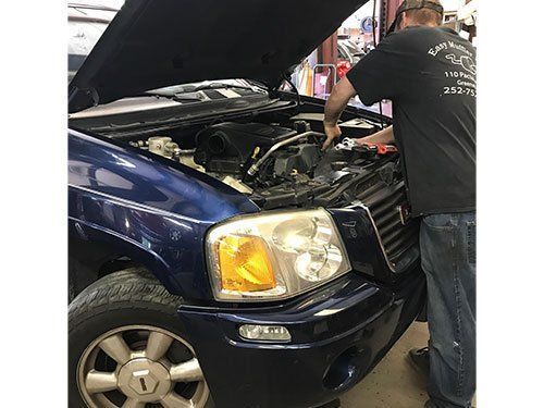 A man is working on the engine of a blue truck.