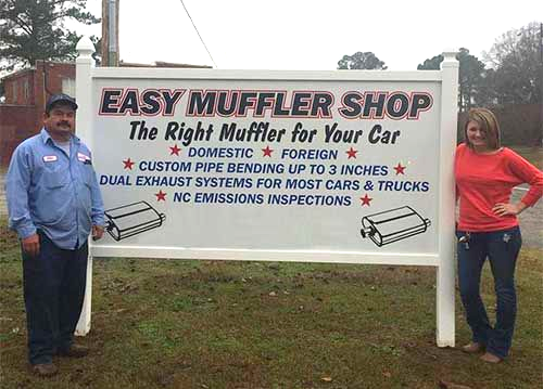 A man and a woman are standing in front of a sign for easy muffler shop.
