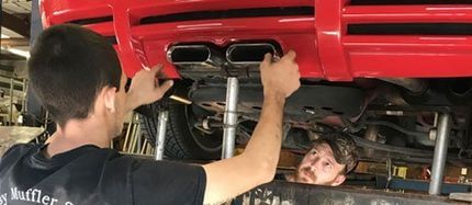 Two men are working on a red car in a garage.
