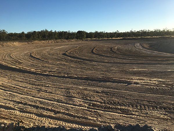A dirt field with tire tracks in it and trees in the background.