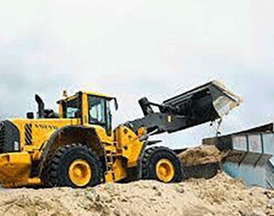 A yellow wheel loader is loading sand into a dumpster.