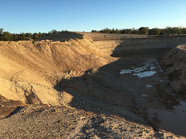 A large hole in the middle of a dirt field with trees in the background.