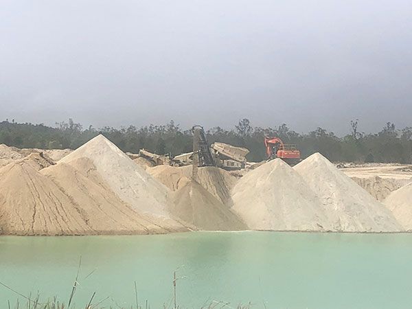 A large pile of sand is sitting next to a body of water.