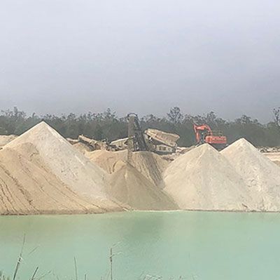 A large pile of sand is sitting next to a body of water.