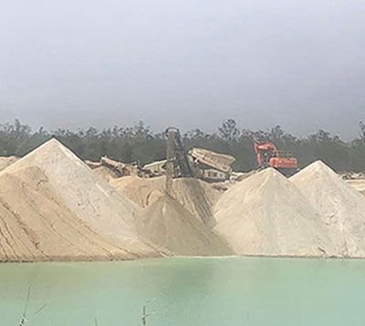 A large pile of sand is sitting next to a body of water.