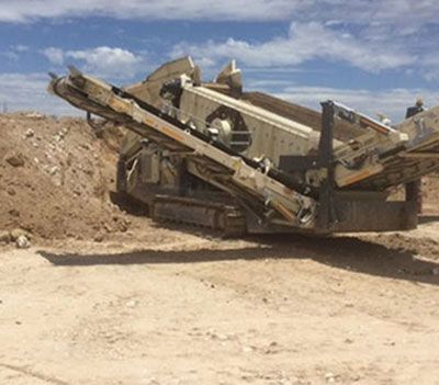 A large machine is sitting in the middle of a dirt field.