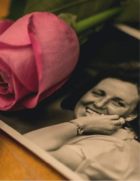 A black and white photo of a woman next to a pink rose