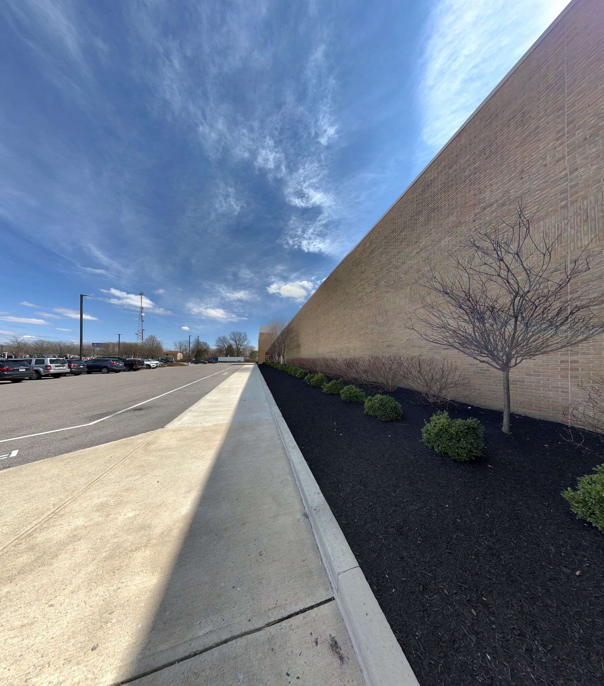 A sidewalk leading to a parking lot with a large wall in the background