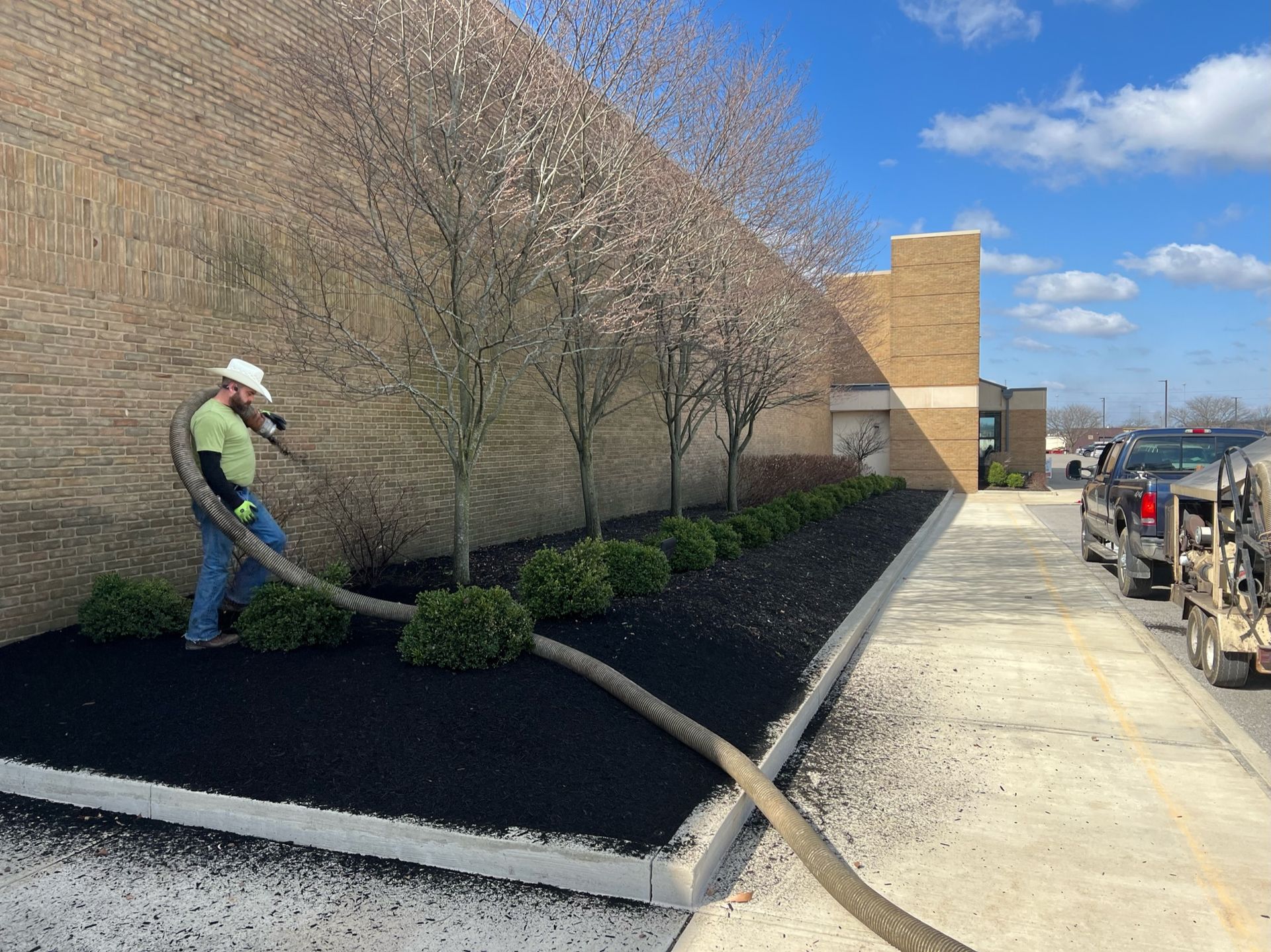A man is blowing mulch into a garden in front of a building.