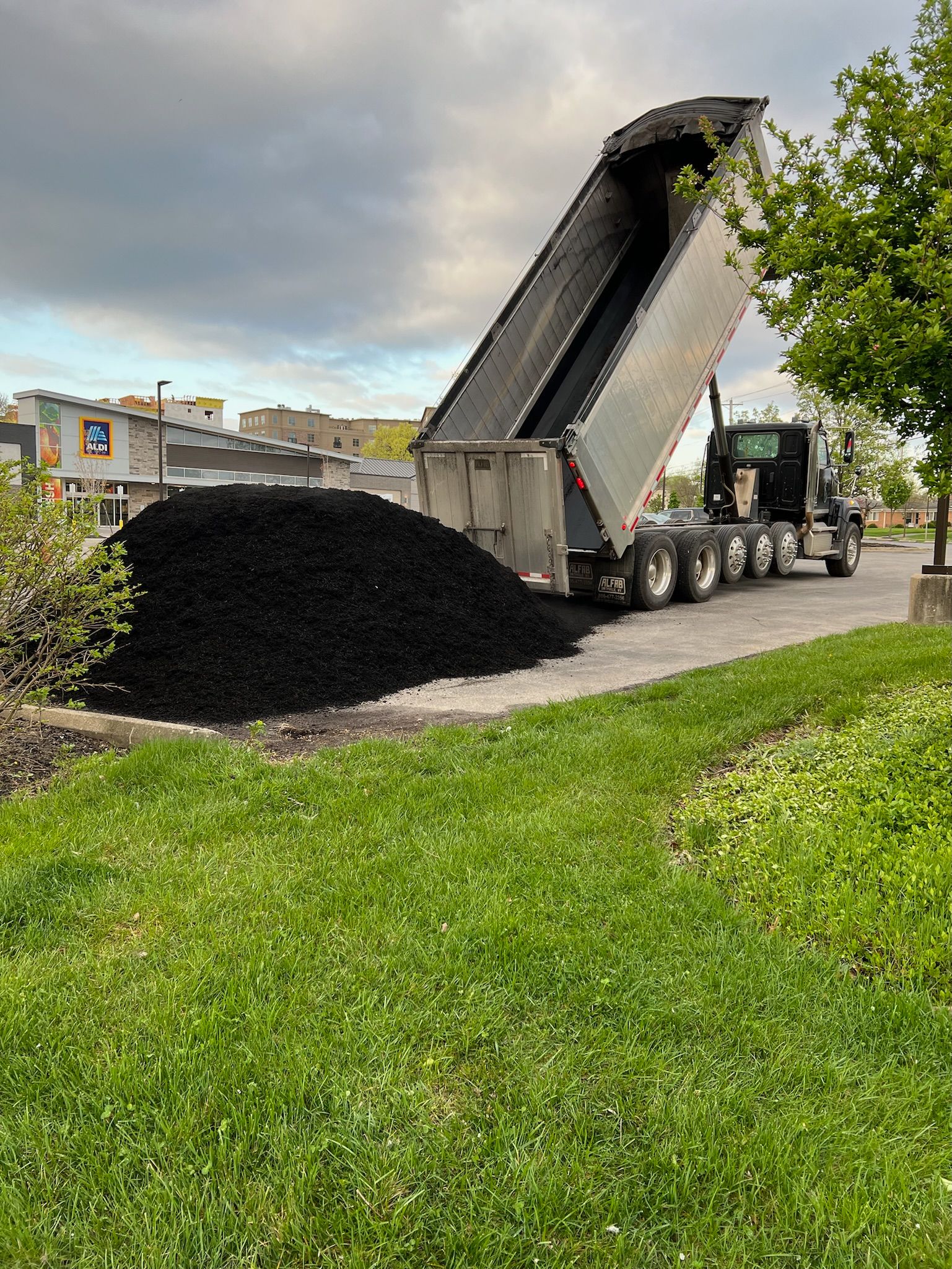 A dump truck is dumping a pile of black dirt on the side of the road.