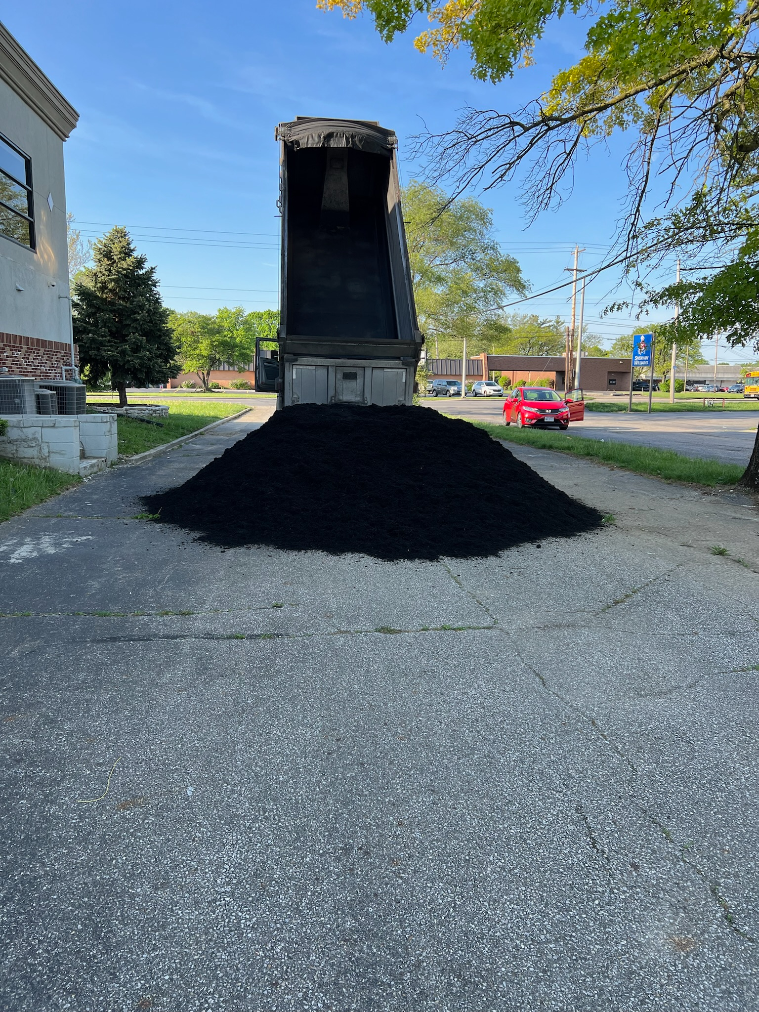 A dump truck is dumping a pile of black mulch on the side of the road.