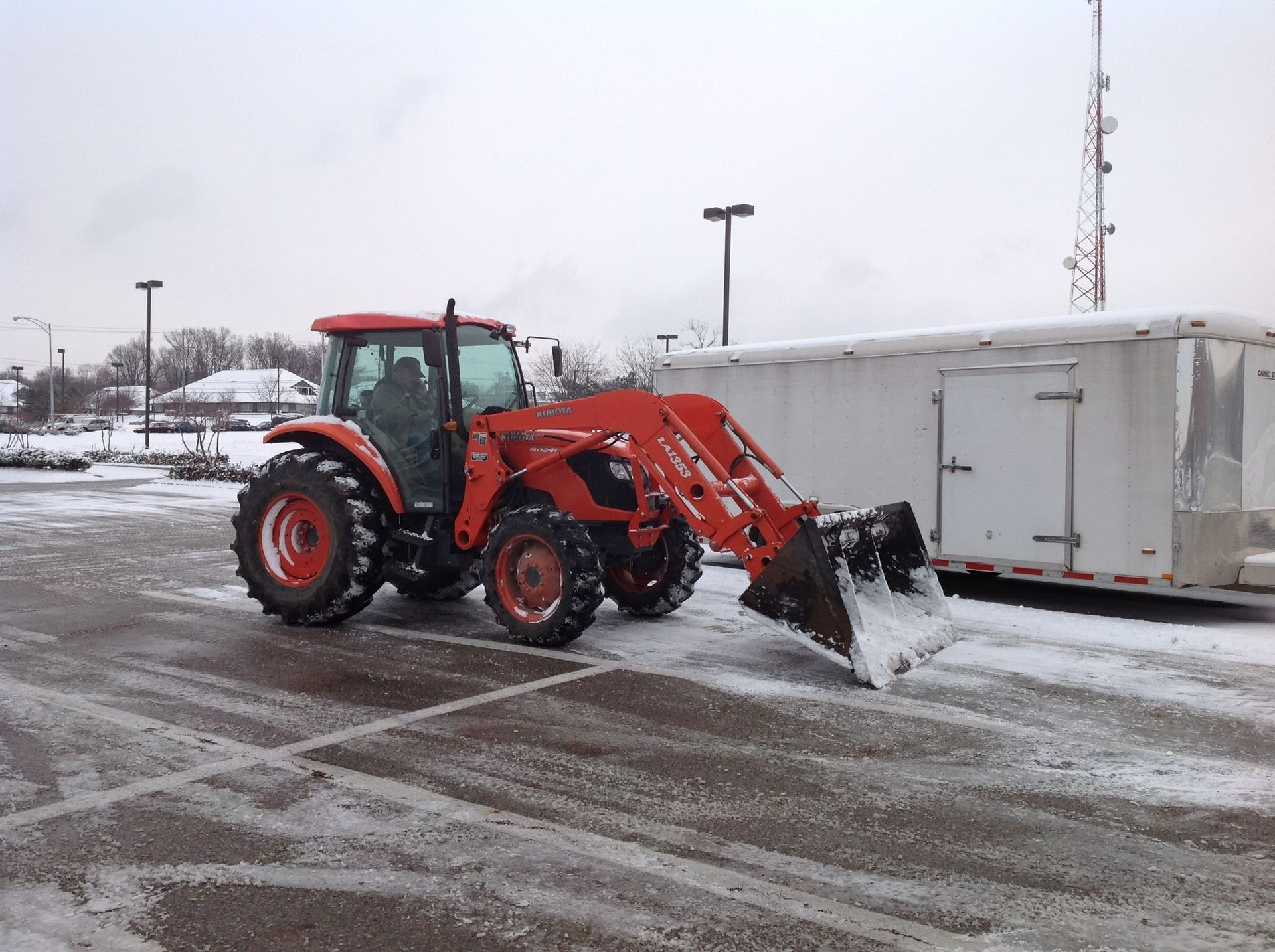 A red tractor is plowing a snowy parking lot