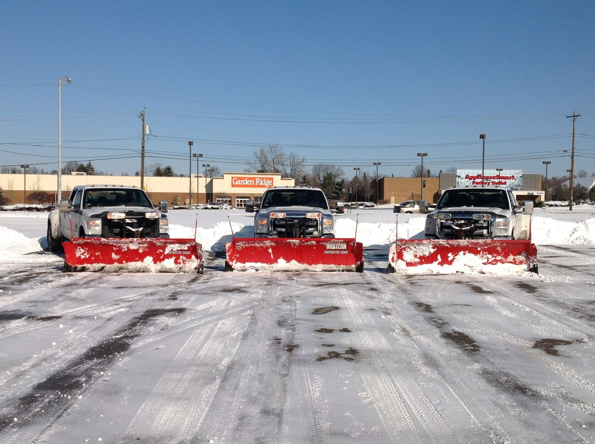 Three snow plows are lined up in a parking lot