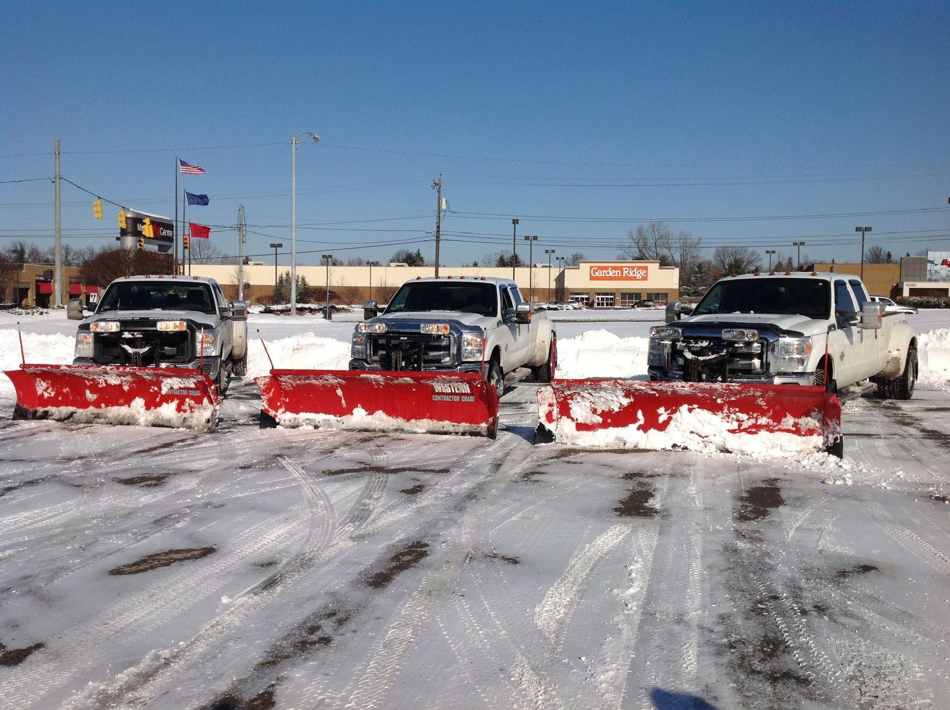 A row of snow plows are parked in a parking lot