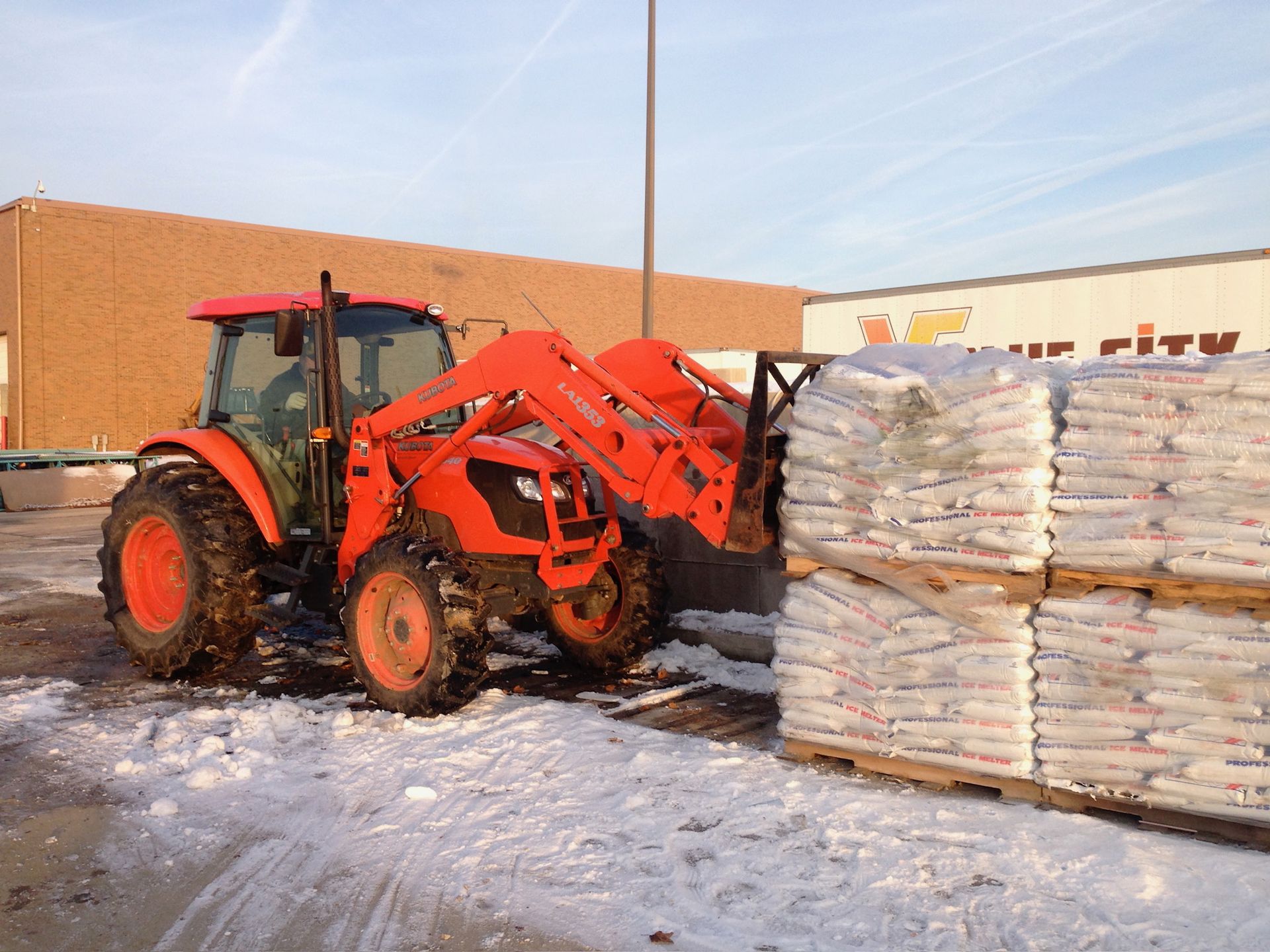An orange tractor is loading a pallet of bags in the snow