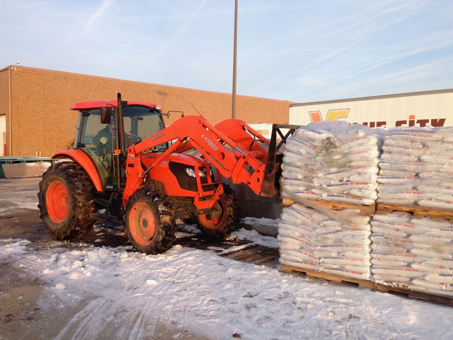 An orange tractor is loading a pallet of bags in the snow