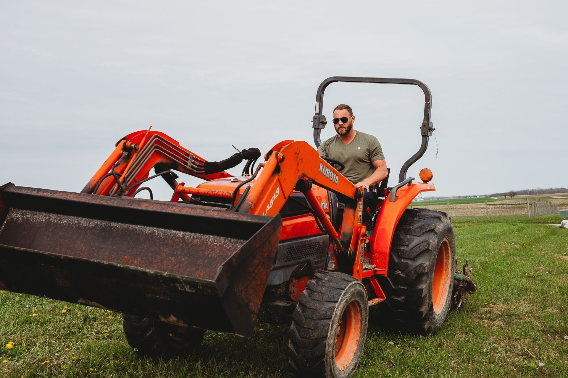 A man is driving an orange tractor in a grassy field.
