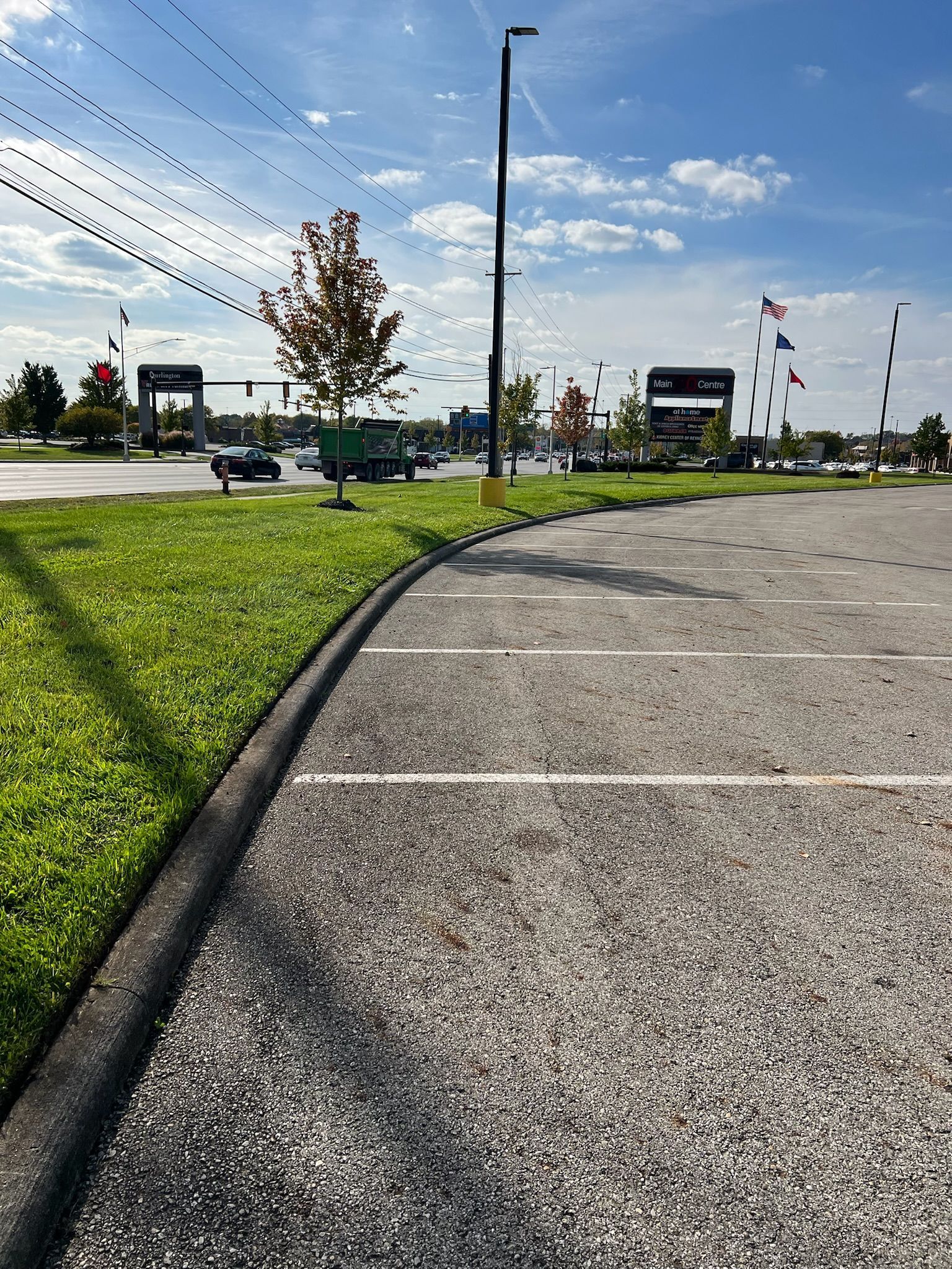 A parking lot with a grassy border and a street in the background.