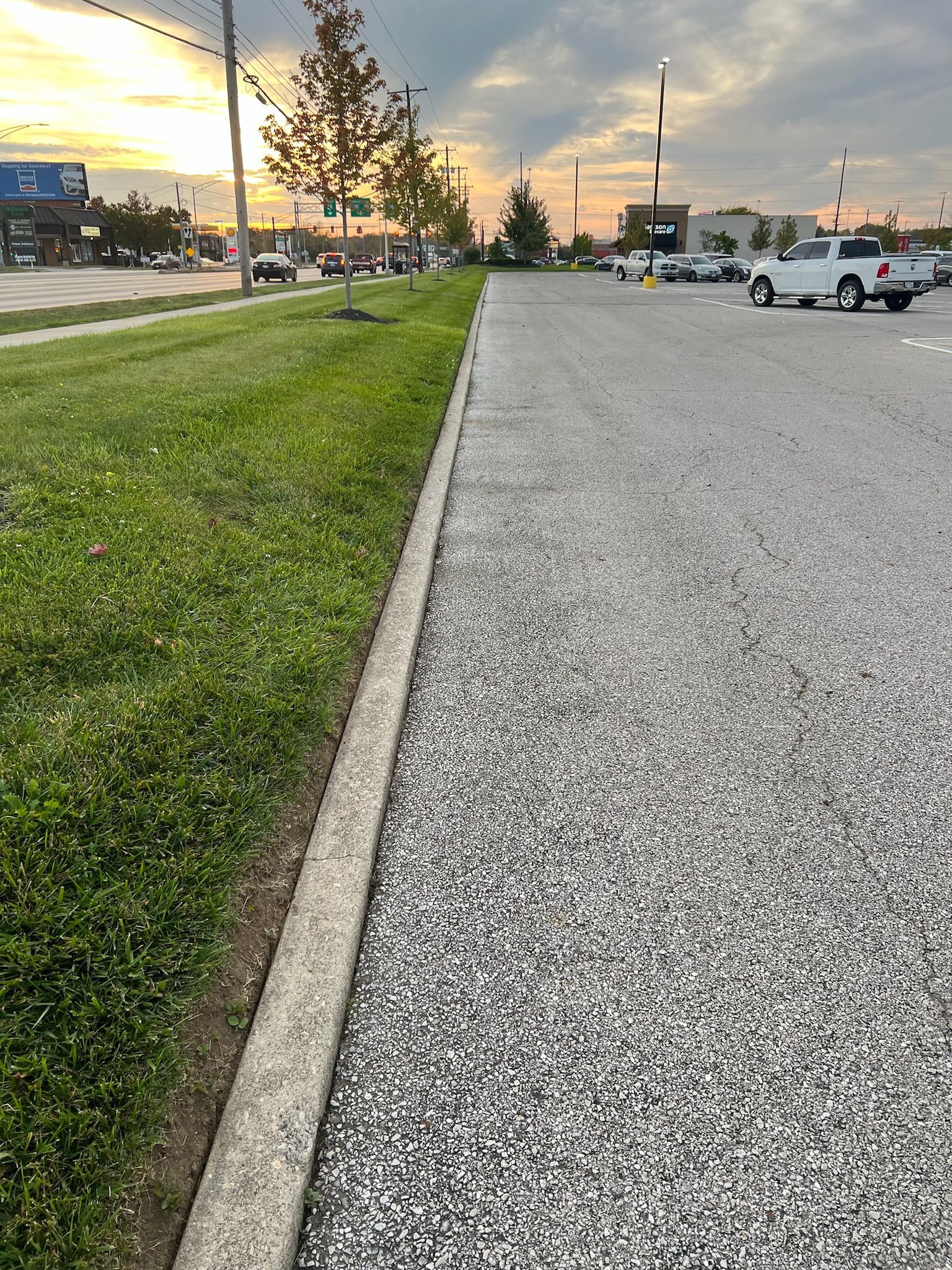 A parking lot with cars parked on the side of the road next to a grassy sidewalk.