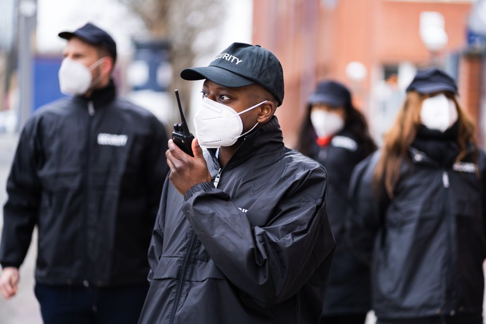 A group of security guards wearing face masks are walking down a street.