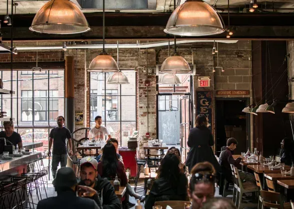 Interior view of a busy restaurant with exposed brick walls, metal lighting fixtures, and patrons dining.