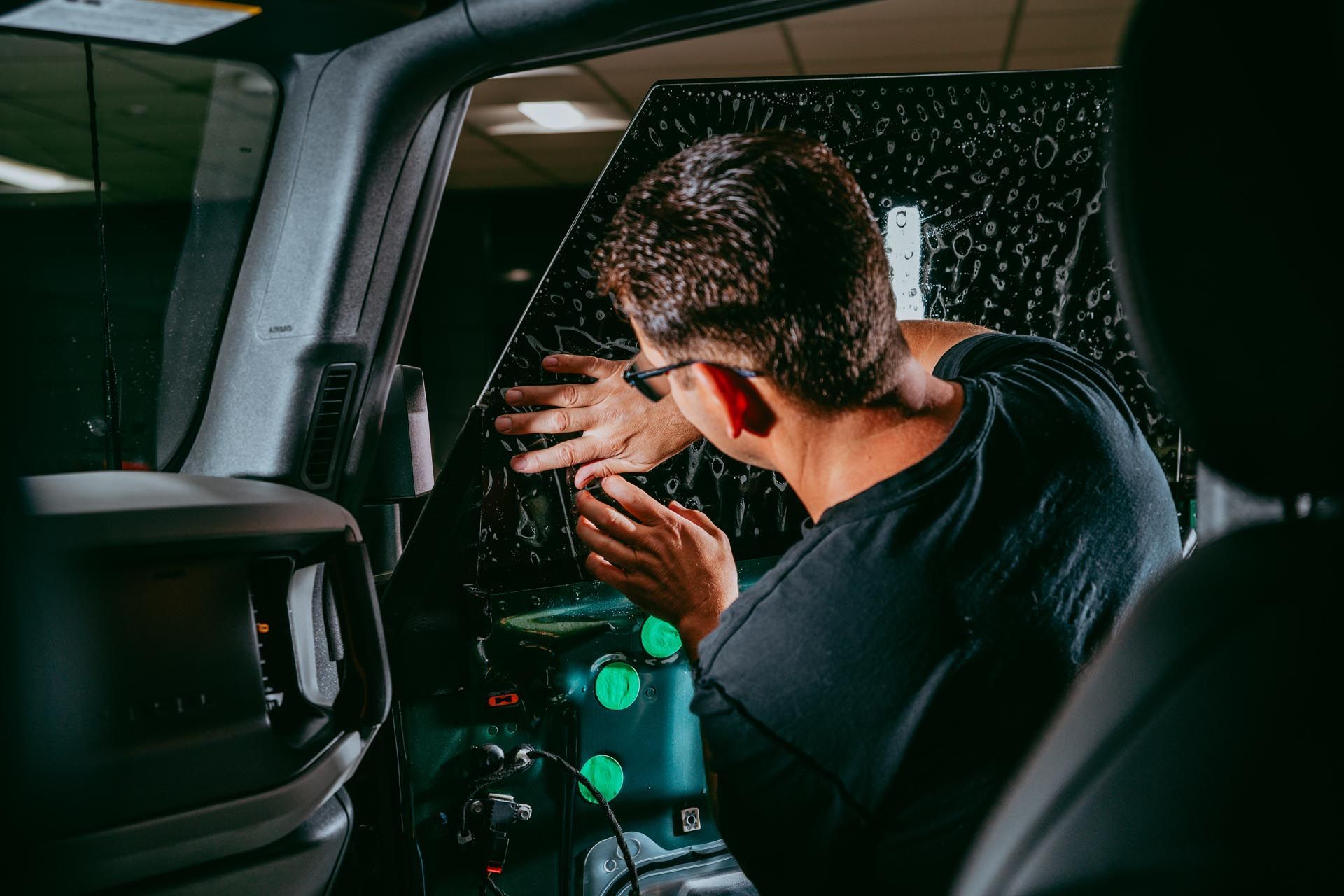 Person applying tint to a car window inside a vehicle. Black tint and interior.