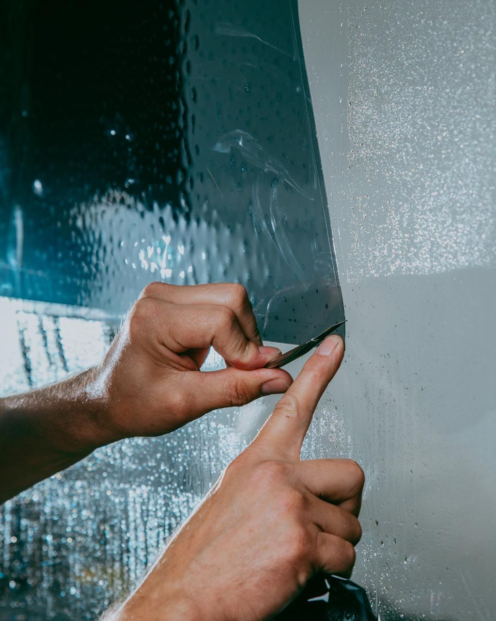 Hands using a blade to trim window tint film.