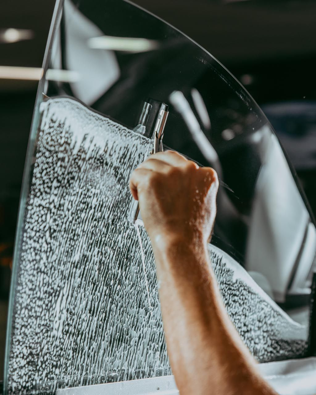 A person's hand applying tint film to a car window with a squeegee.
