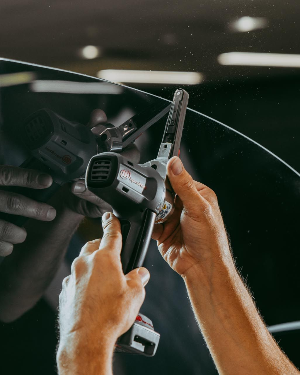 Hands using a power tool on a curved surface, possibly glass, in a workshop setting.