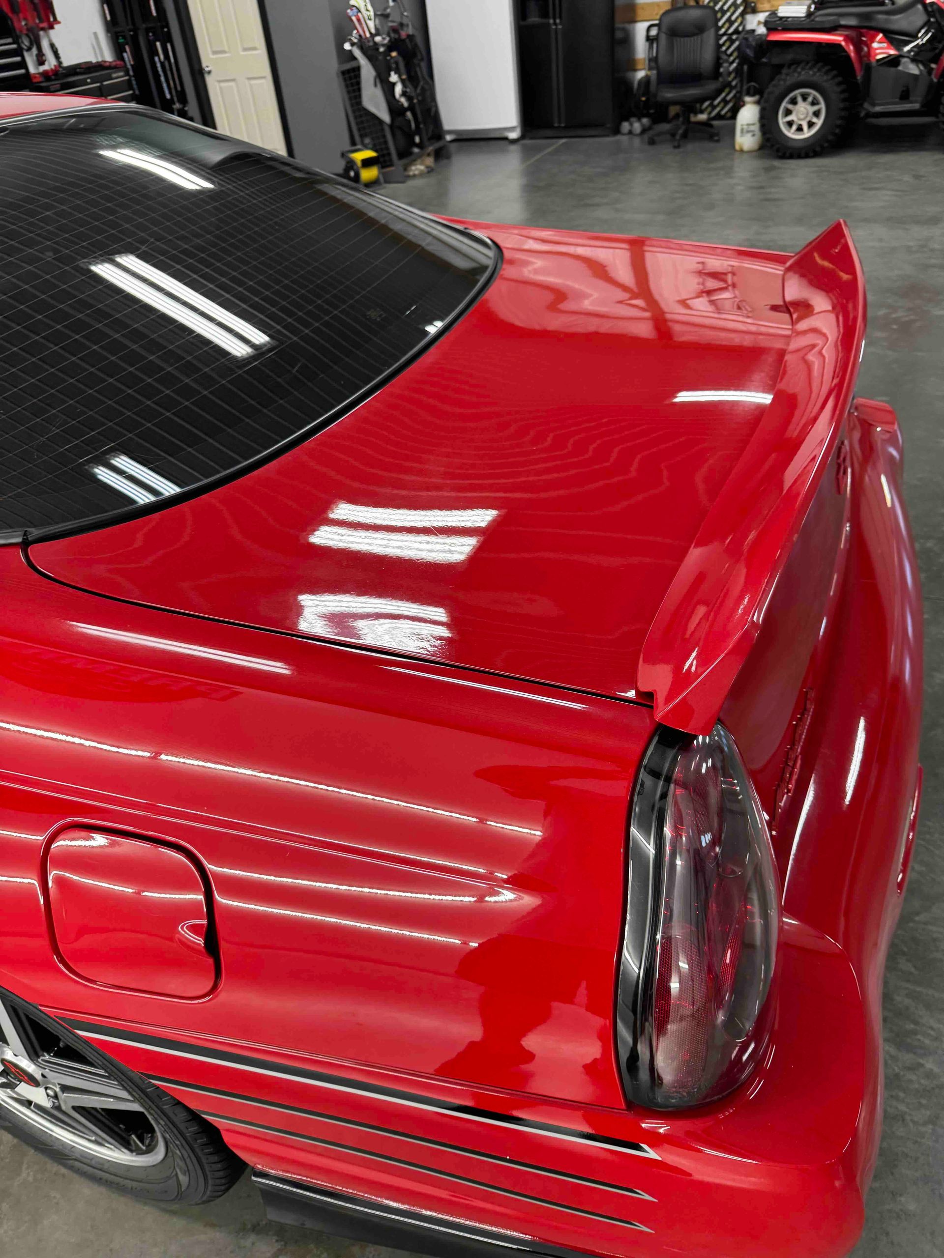 Red car with a spoiler, tinted windows, and a black taillight.