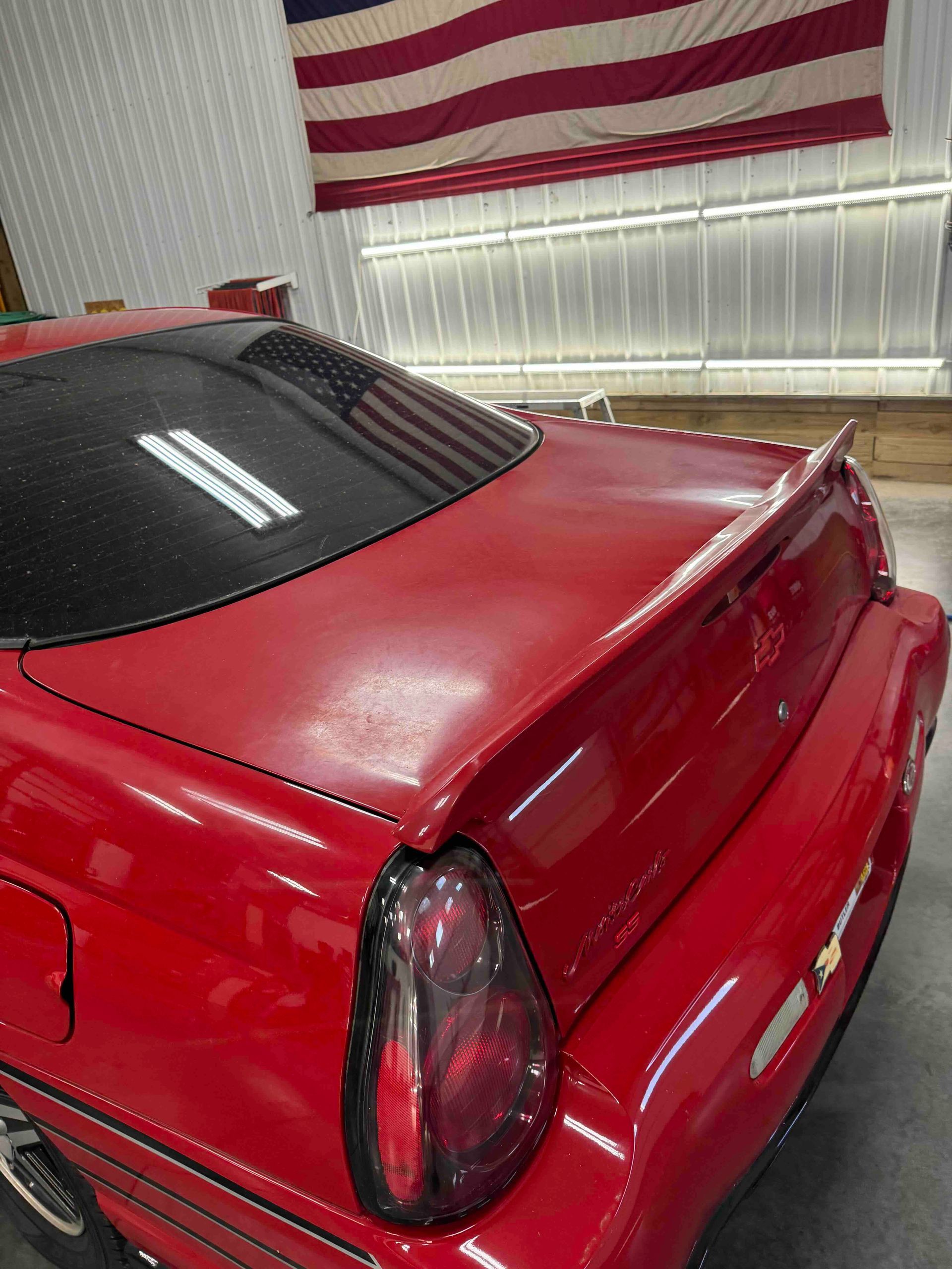 Red car with black tinted taillight and a spoiler, with an American flag in the background.