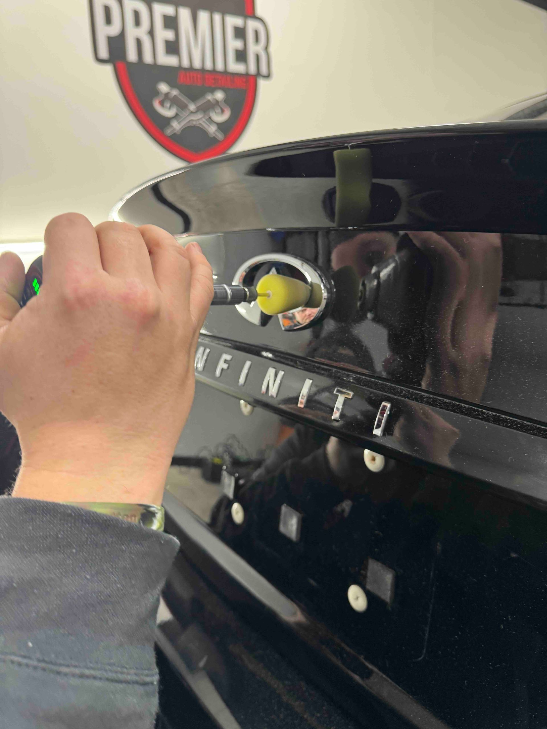 Person using a tool to remove the Infiniti emblem from a black car's trunk.