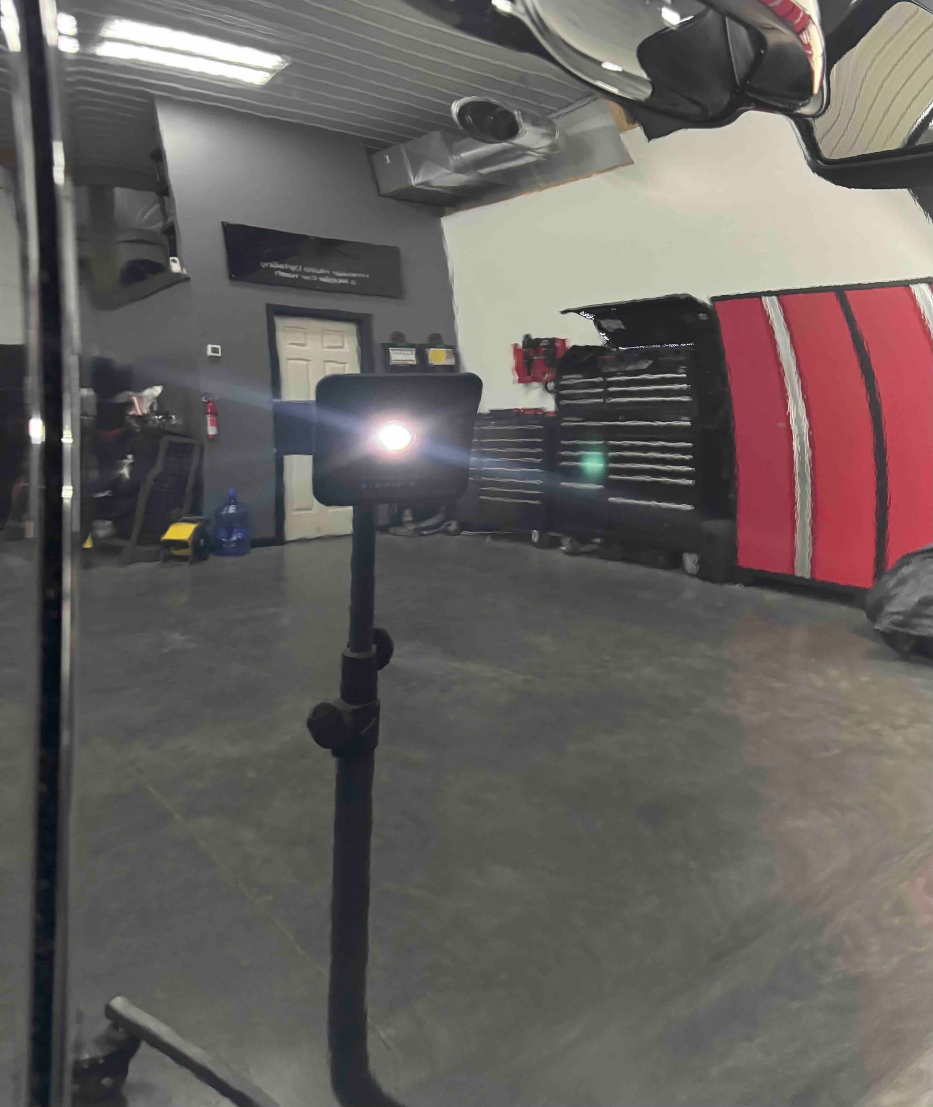 Bright spotlight on a tripod in a garage with tools and a red vehicle.