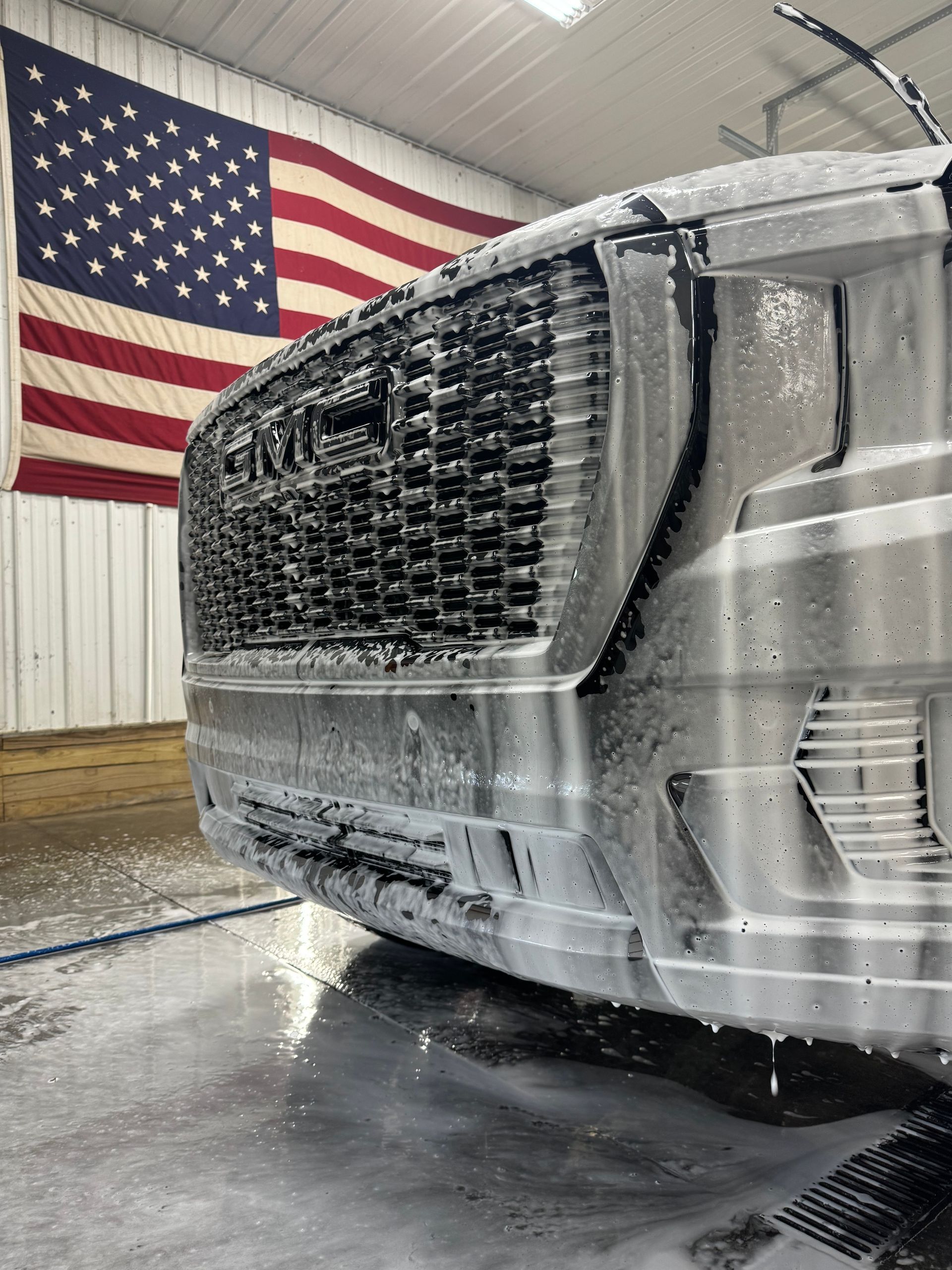 Truck front covered in soapy foam, with American flag in the background.