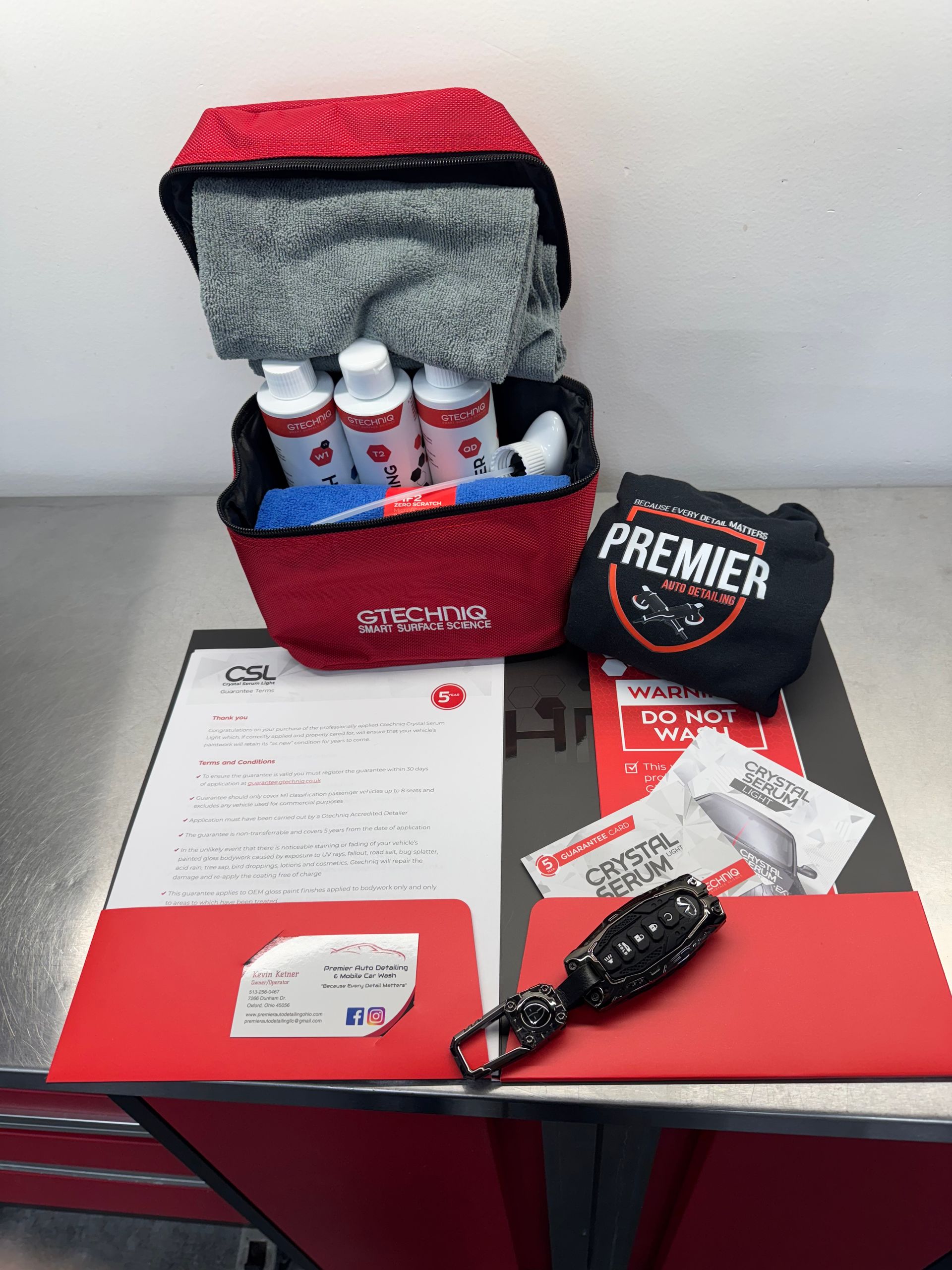 Red cleaning kit with supplies, Premier logo, on a metal surface. Includes bottles, towel, and paperwork.