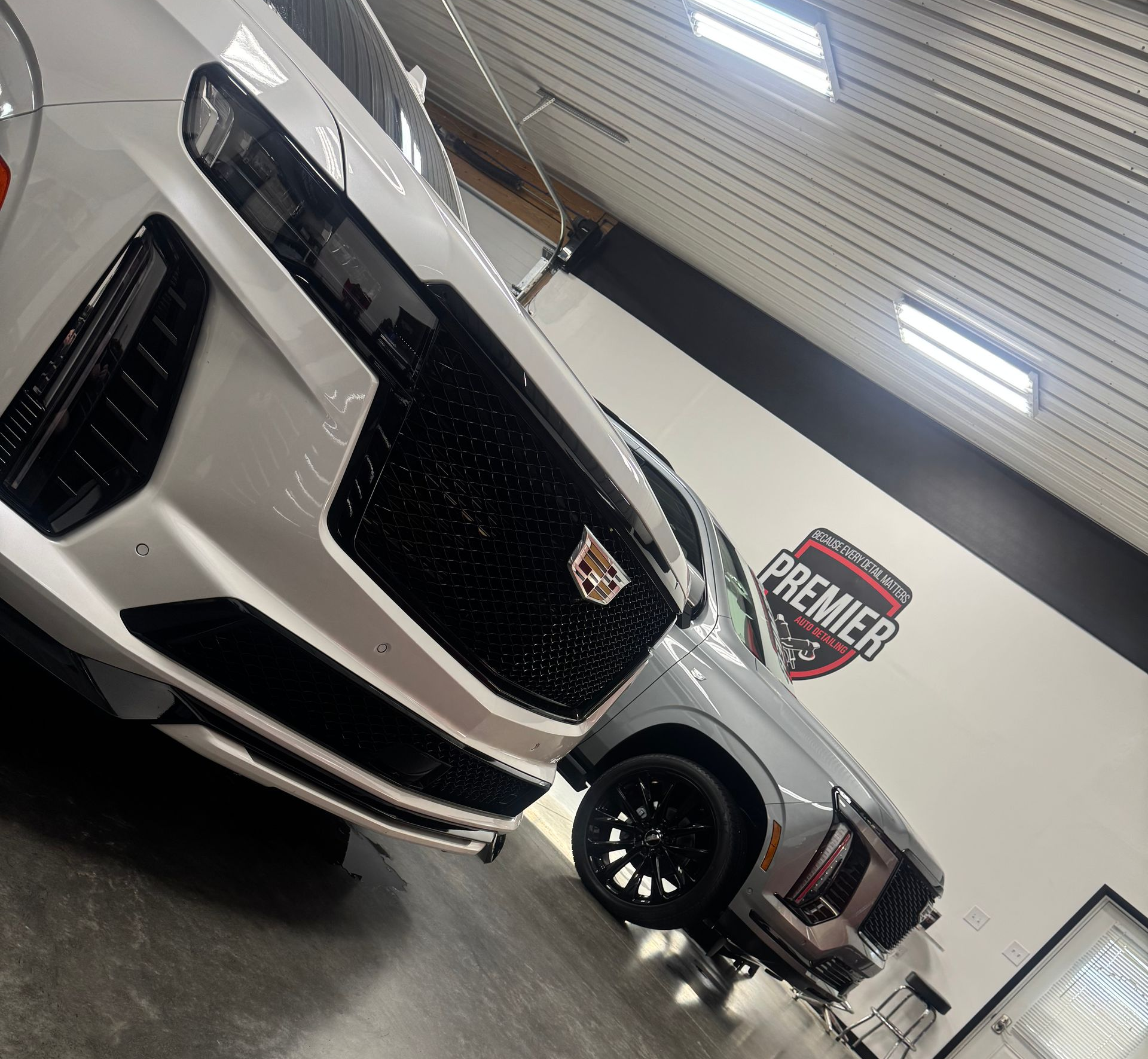 White Cadillac SUV being washed at Premier Detailing in a shop with gray floors.