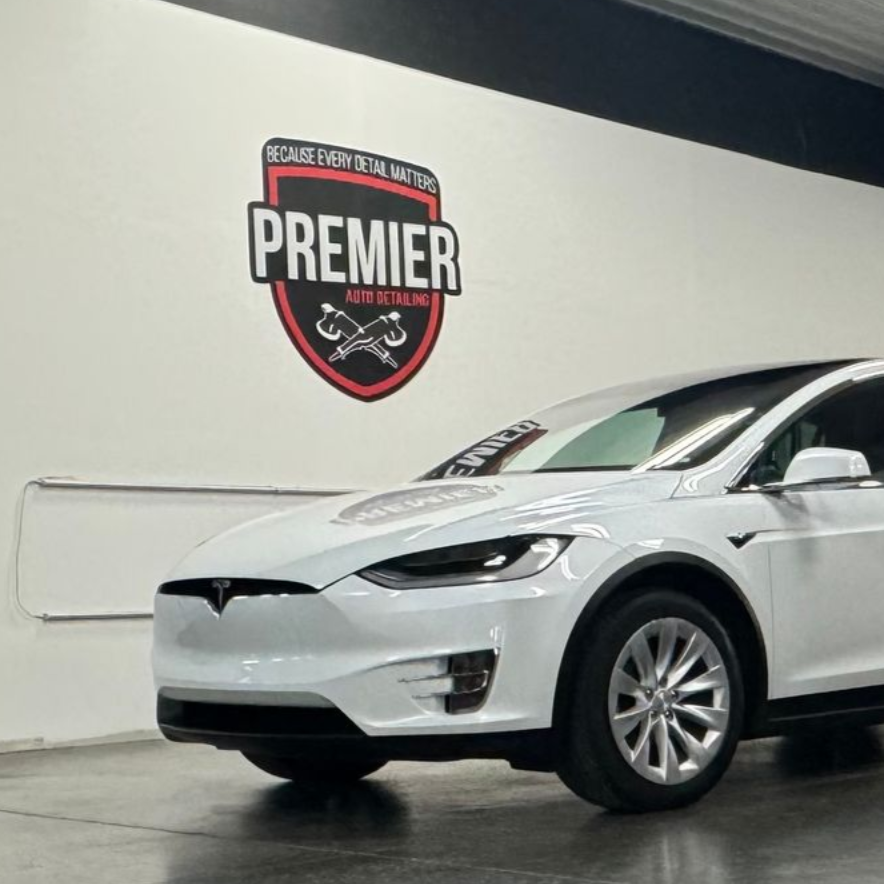 A white Tesla and a black SUV parked inside a garage. A logo is visible on the wall.