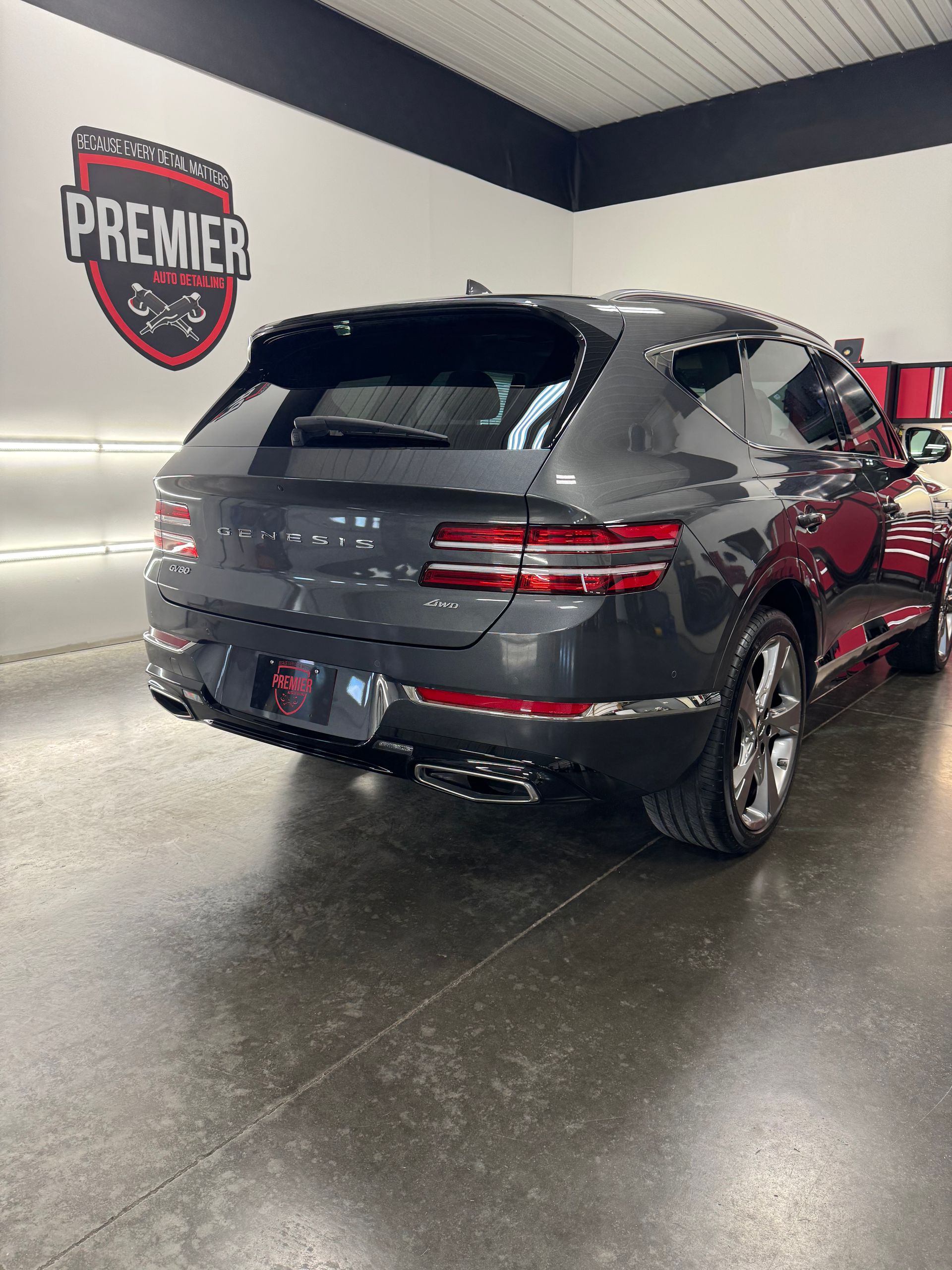 Gray Genesis GV70 SUV in a car detailing shop. The Premier logo is on the wall.