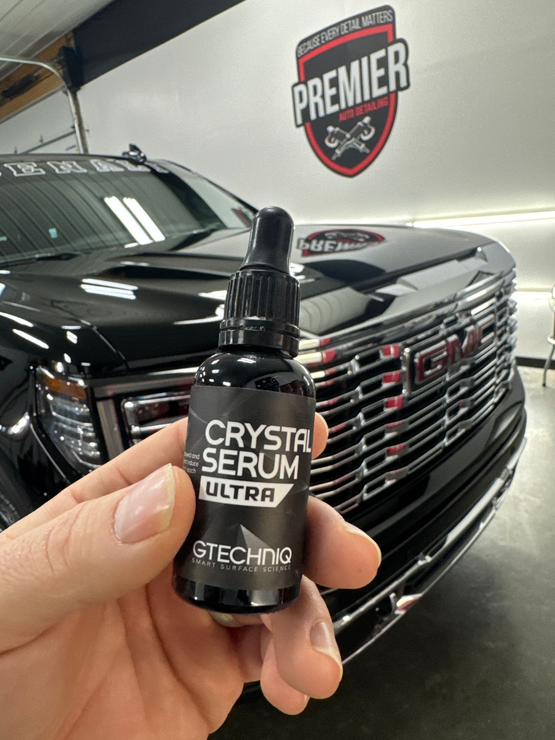 Hand holding a bottle of Gtechniq Crystal Serum Ultra car ceramic coating in front of a black GMC truck.