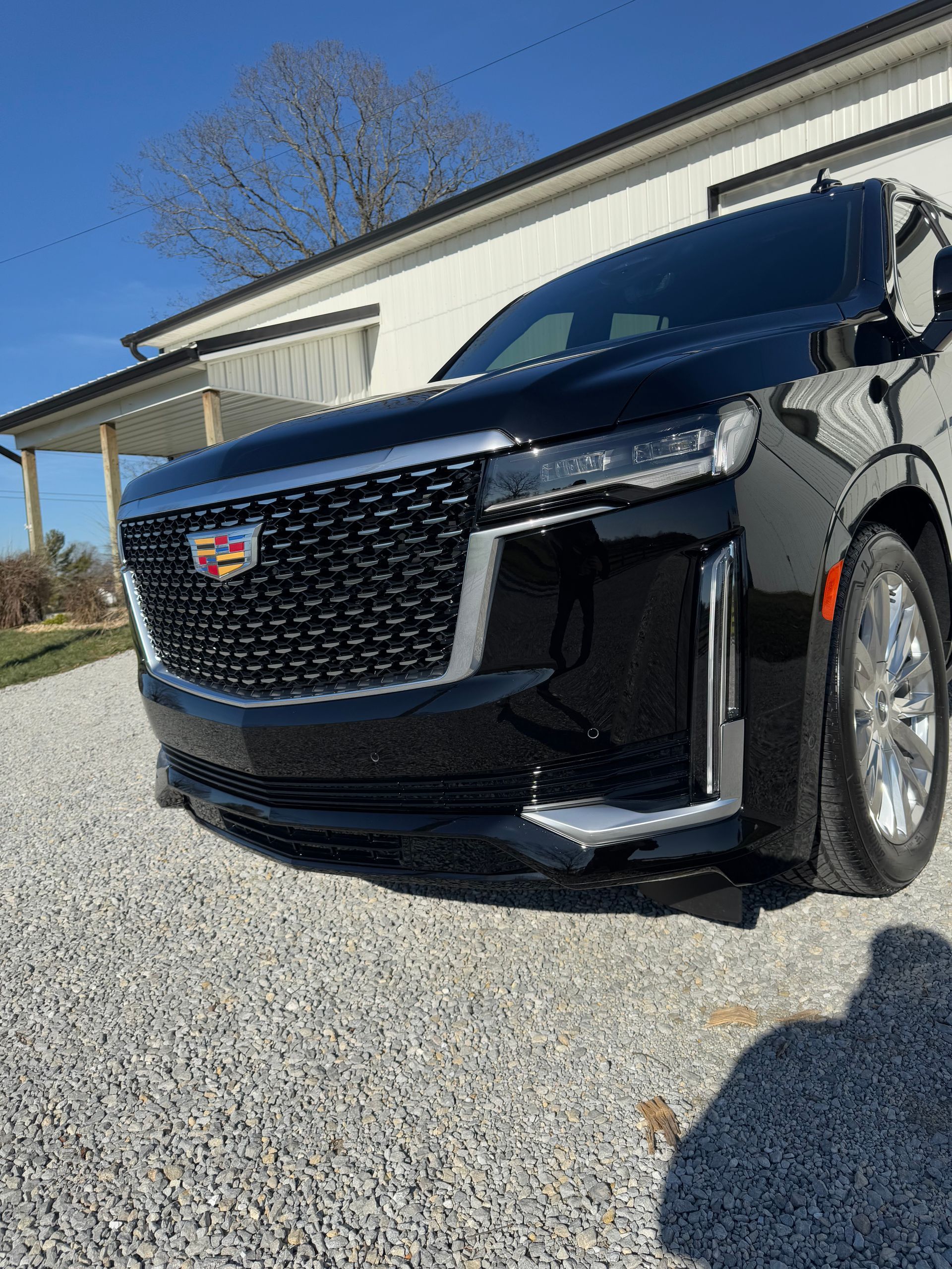 Black Cadillac Escalade parked on gravel, front view. Chrome accents, daytime.