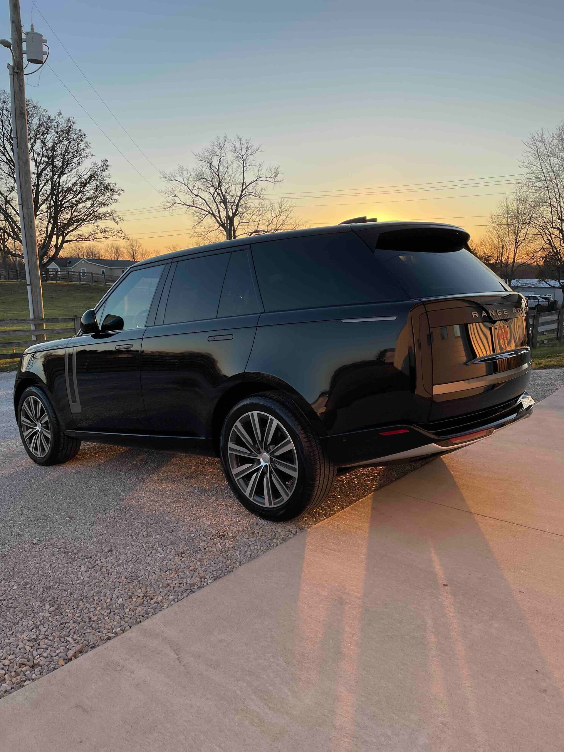Black Range Rover SUV parked outdoors on a paved area with a sunset background.