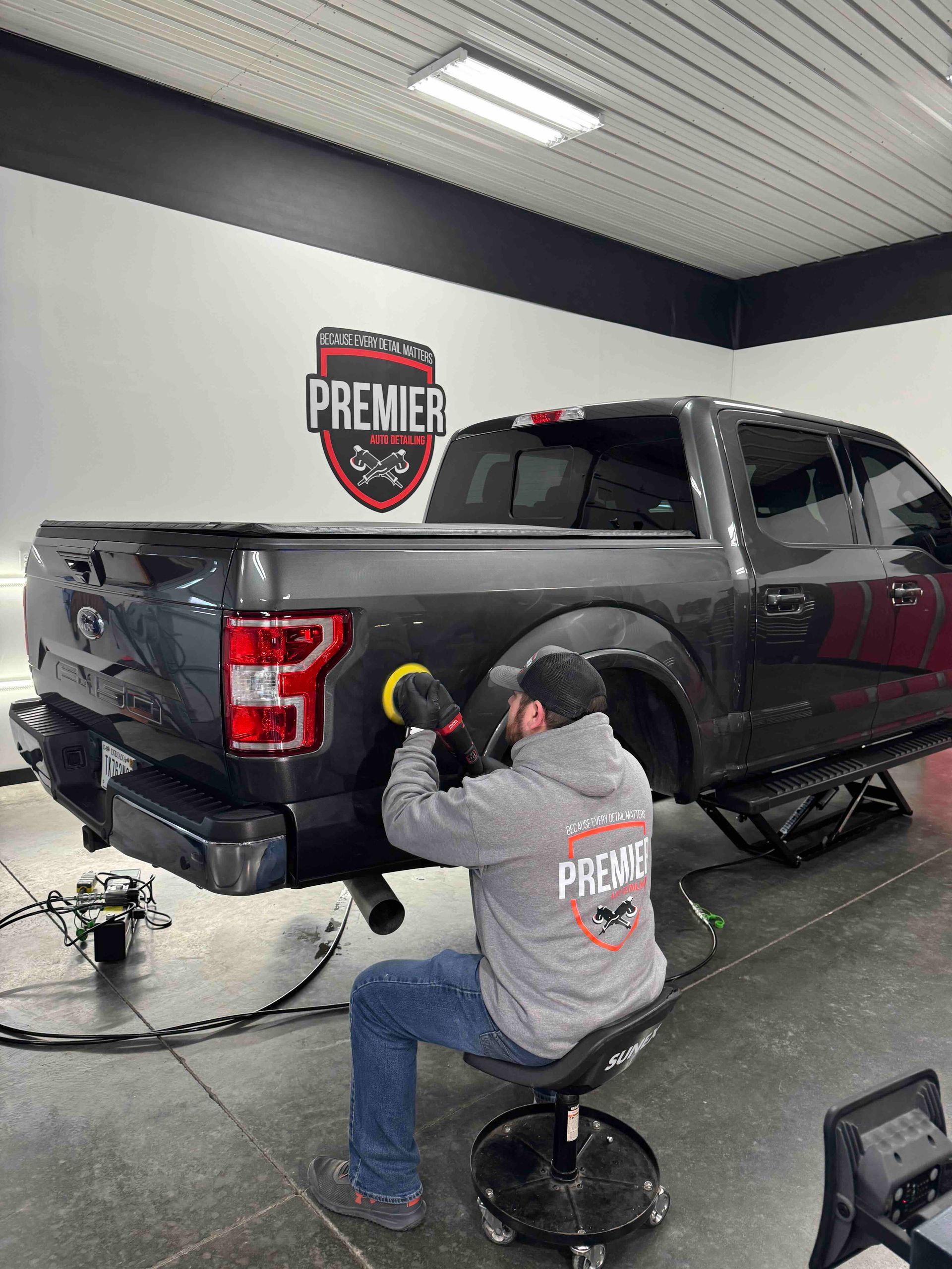 Man polishing dark pickup truck in auto shop.