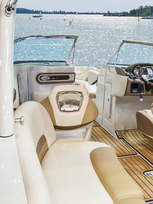 White sailboat docked at a marina with a black stripe, blue canopy, and tall buildings in the background.